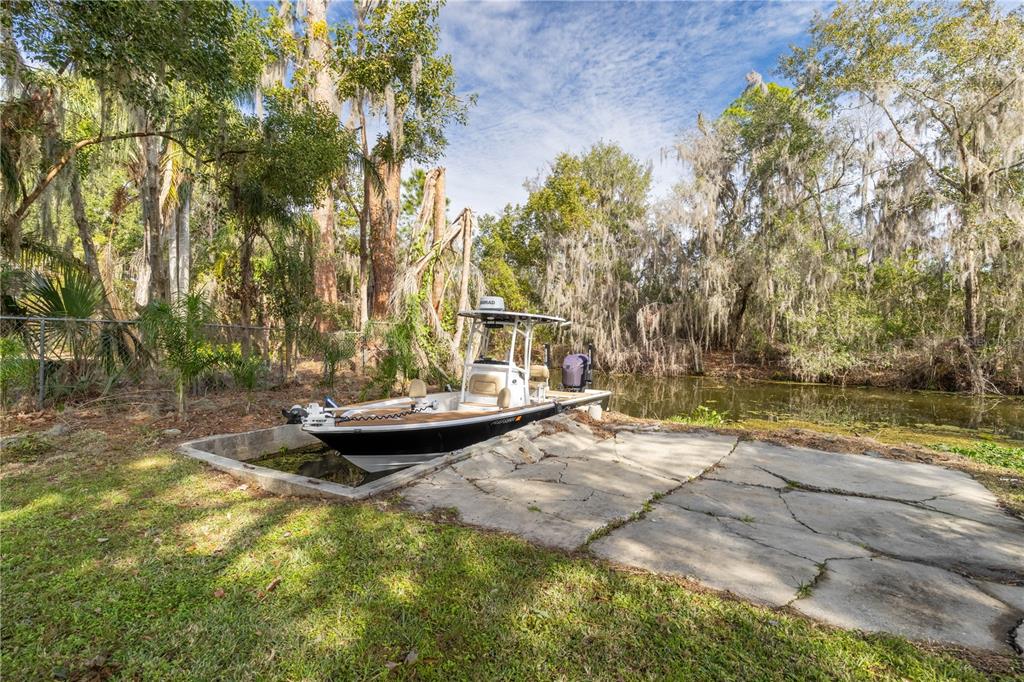 A motorboat is docked at a concrete boat ramp beside a wooded canal — 11807 OCKLAWAHA DRIVE, LEESBURG, FL