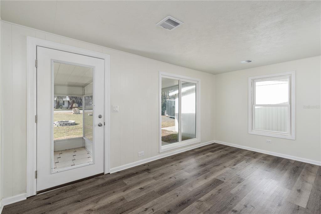 A room with white walls, wood-look flooring, a glass-paneled door, and two windows — 11807 OCKLAWAHA DRIVE, LEESBURG, FL