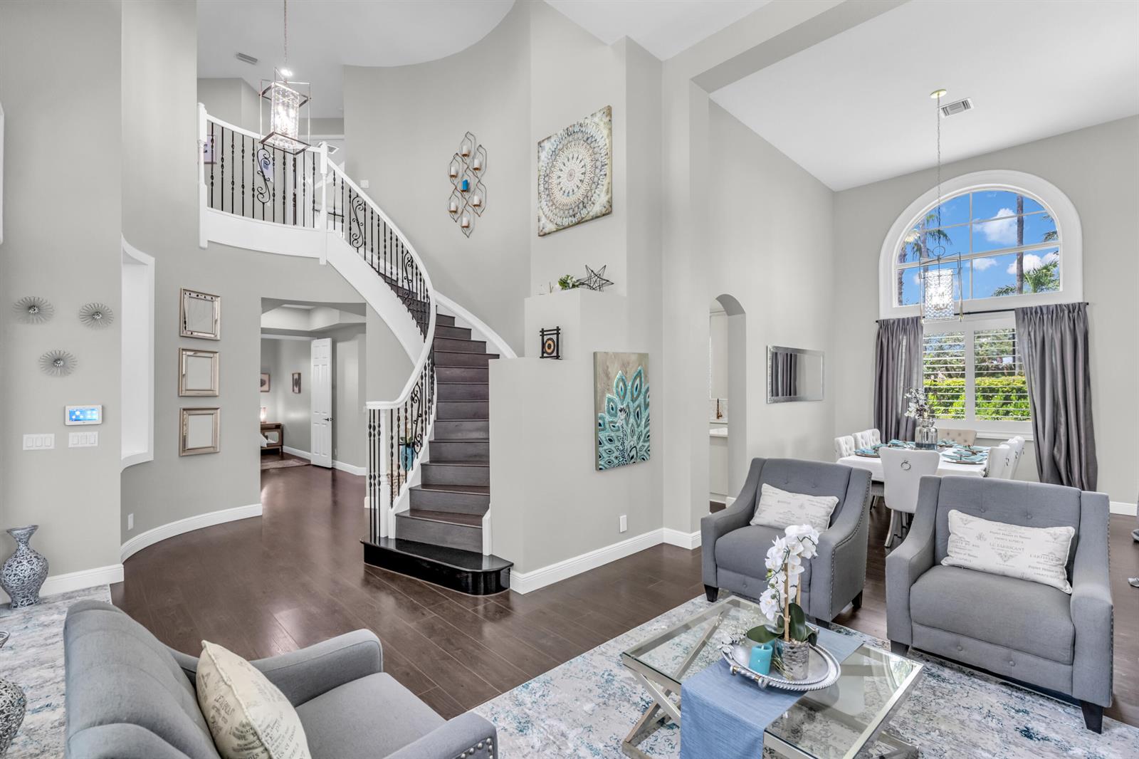 A living room with a curved staircase, hardwood floors, and a large arched window — 4661 Manderly Drive, Wellington FL 33449, WELLINGTON, FL