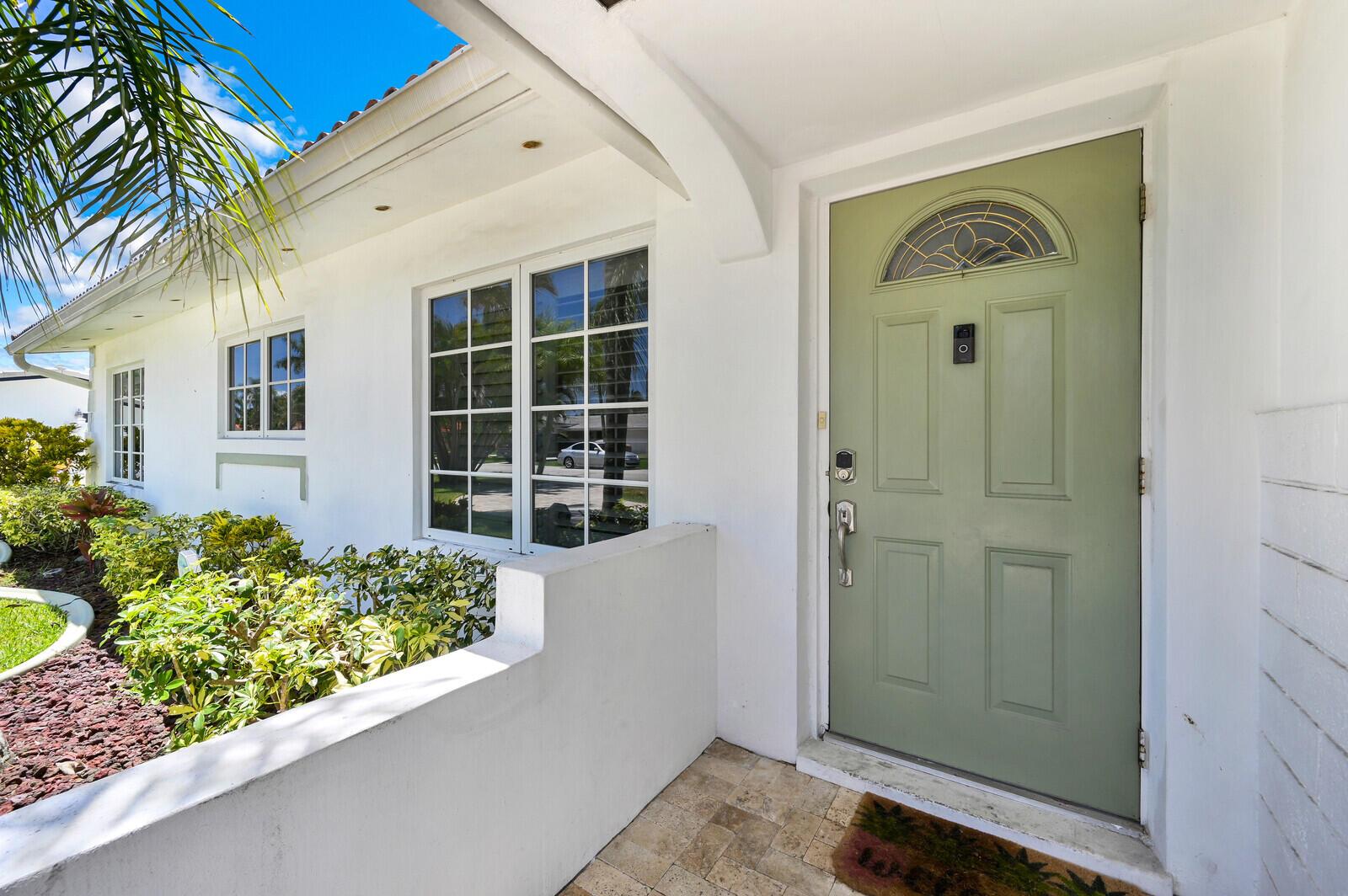 A sage green front door with a window sits beside a white house exterior — 904 SE 12th Street, Deerfield Beach FL 33441, DEERFIELD BEACH, FL