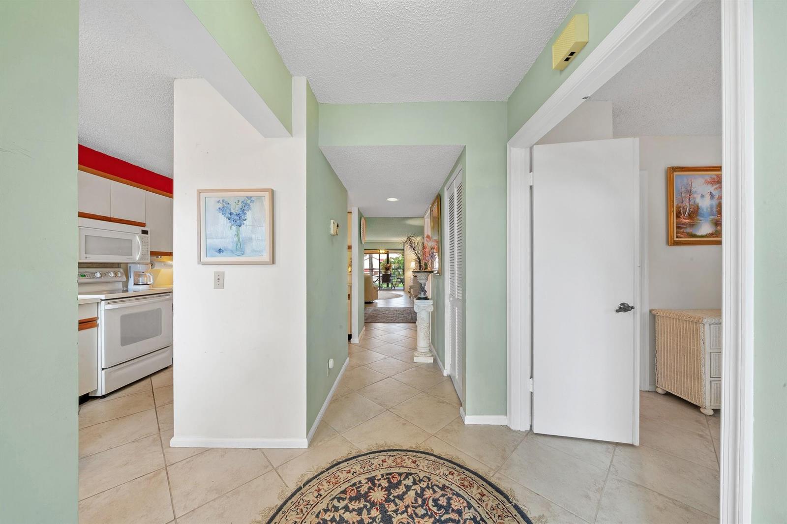 A hallway with light green walls and tile flooring leads toward a bright living area — 5306 Cedar Lake Drive # 203, Boynton Beach FL 33437, BOYNTON BEACH, FL