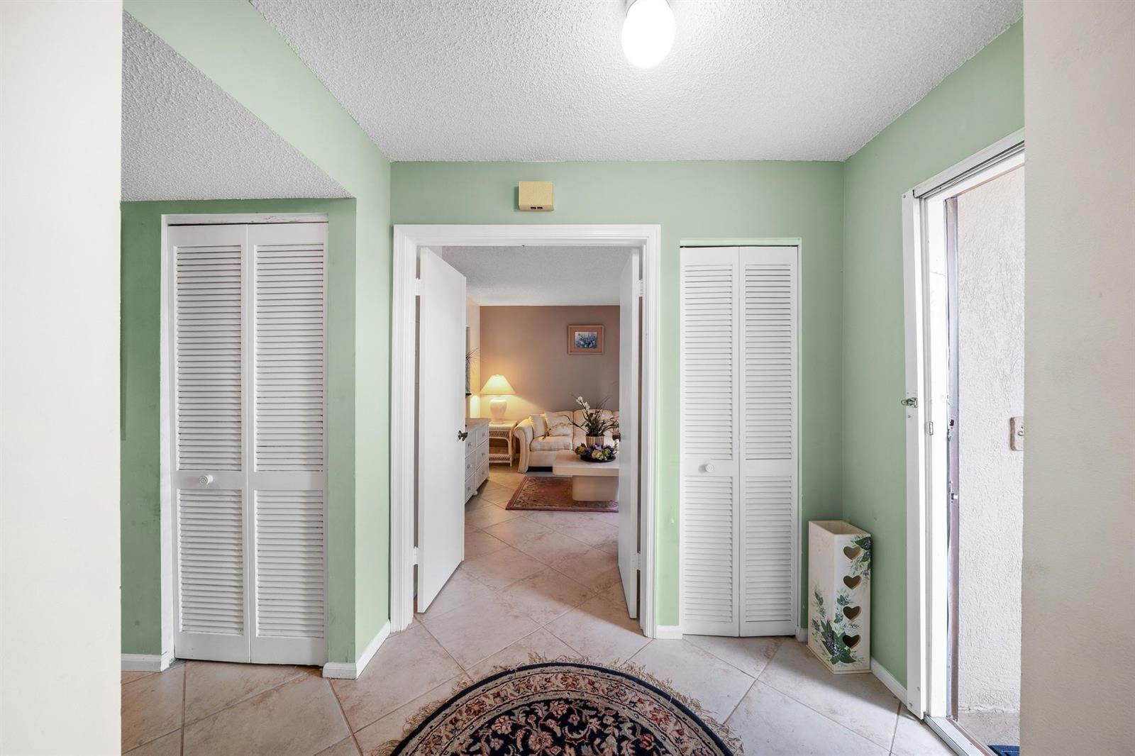 An entryway with light green walls, tile flooring, and two white louvered closet doors — 5306 Cedar Lake Drive # 203, Boynton Beach FL 33437, BOYNTON BEACH, FL