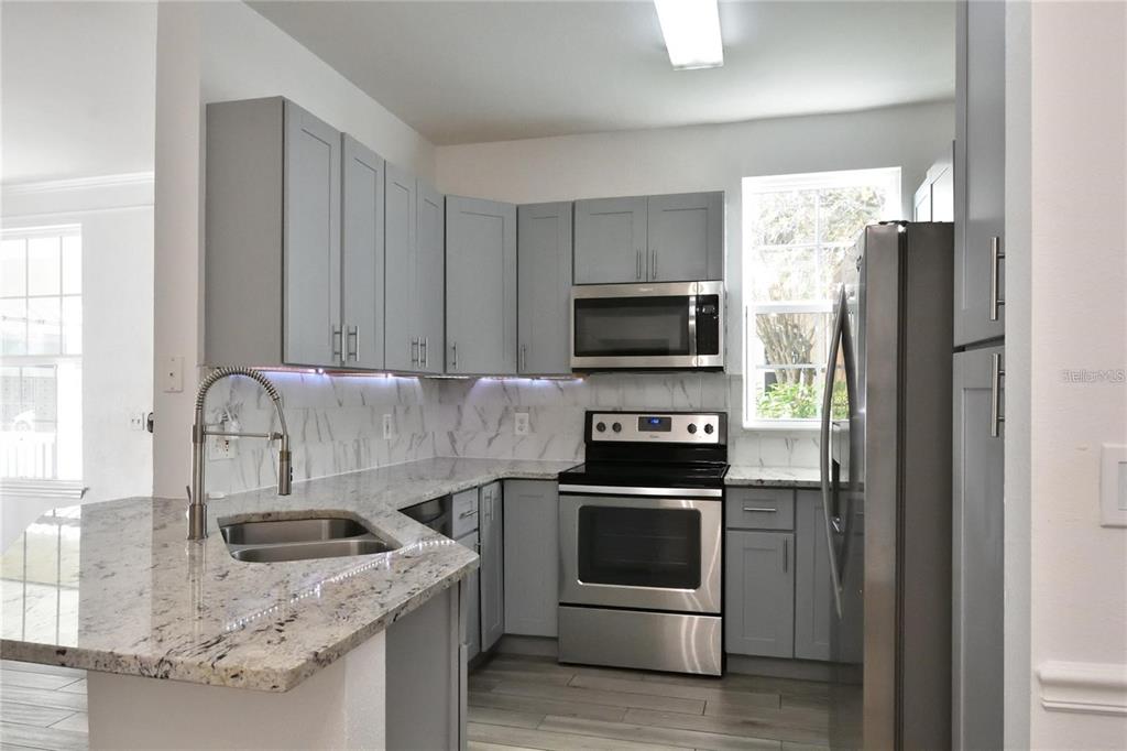 A kitchen features gray cabinets, granite countertops, stainless steel appliances, and a marble-look backsplash — 3396 PARKCHESTER SQUARE BOULEVARD UNIT 104, ORLANDO, FL