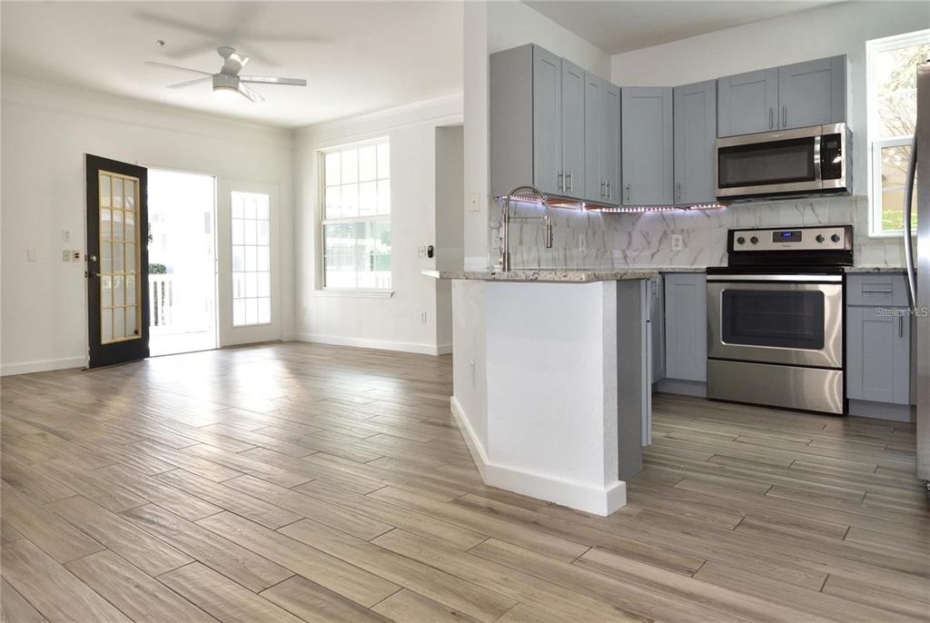 A kitchen with gray cabinets and stainless steel appliances opens to a living area — 3396 PARKCHESTER SQUARE BOULEVARD UNIT 104, ORLANDO, FL