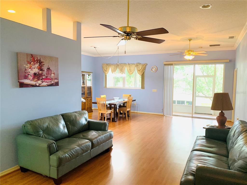 A living room with light blue walls, wood flooring, two leather sofas, and a dining area — 809 SUMMIT GREENS BOULEVARD, CLERMONT, FL