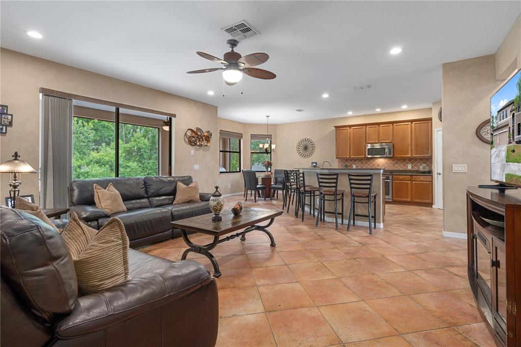 An open-concept living room and kitchen featuring tile floors, leather sofas, and wooden cabinetry — 14807 PRINCEWOOD LANE, LAND O LAKES, FL