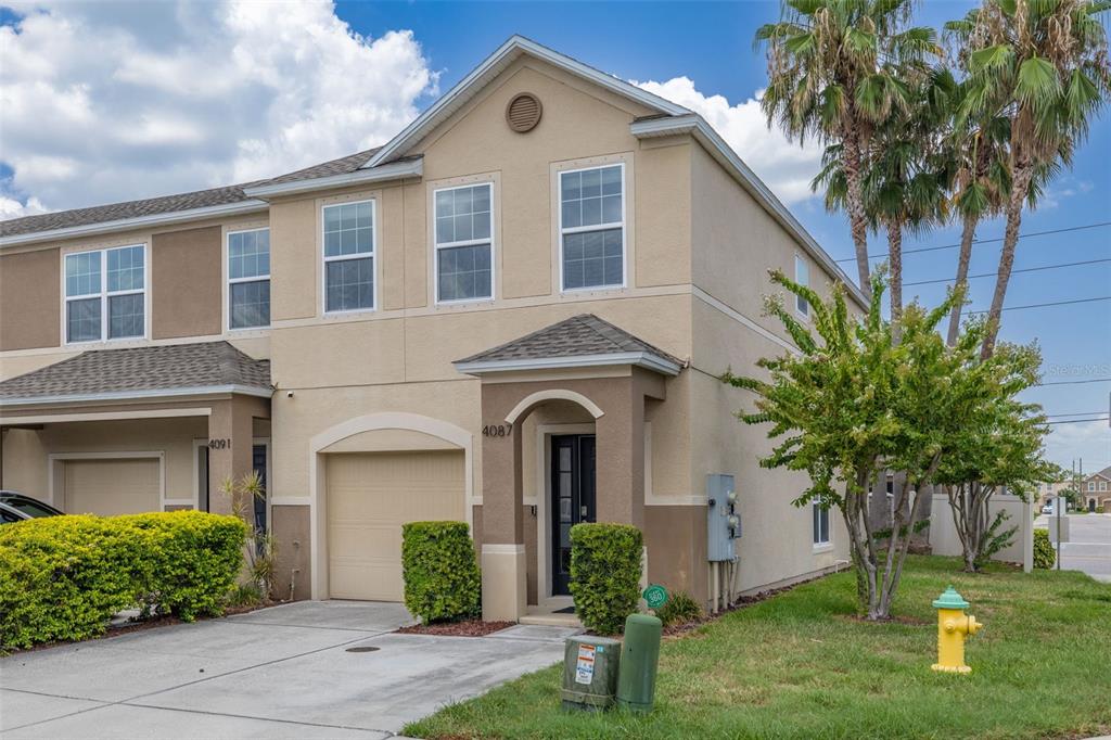 A two-story townhouse with a beige stucco exterior, a single-car garage, and a small lawn — 4087 69TH TERRACE N, PINELLAS PARK, FL