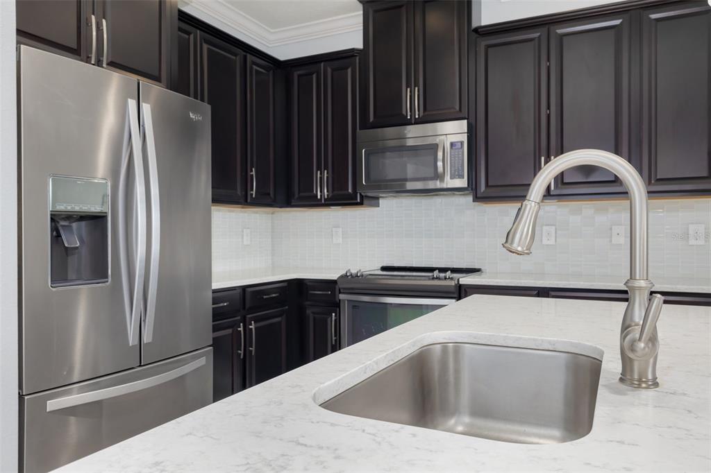 A kitchen features dark wood cabinets, stainless steel appliances, and a white marble-look countertop island — 4087 69TH TERRACE N, PINELLAS PARK, FL