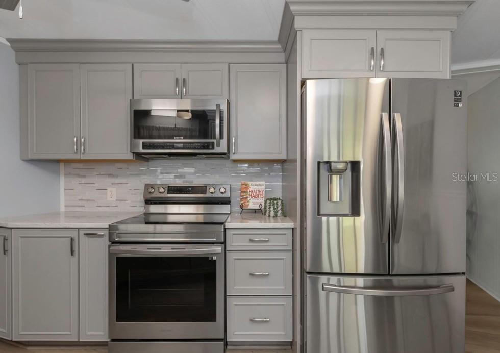 A kitchen features gray cabinets, stainless steel appliances, and a light-colored tiled backsplash — 198 PHILADELPHIA BOULEVARD UNIT 11, PALM HARBOR, FL