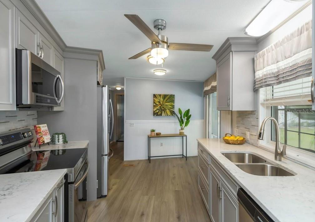 A galley kitchen features gray cabinets, stainless steel appliances, and light wood-look flooring — 198 PHILADELPHIA BOULEVARD UNIT 11, PALM HARBOR, FL