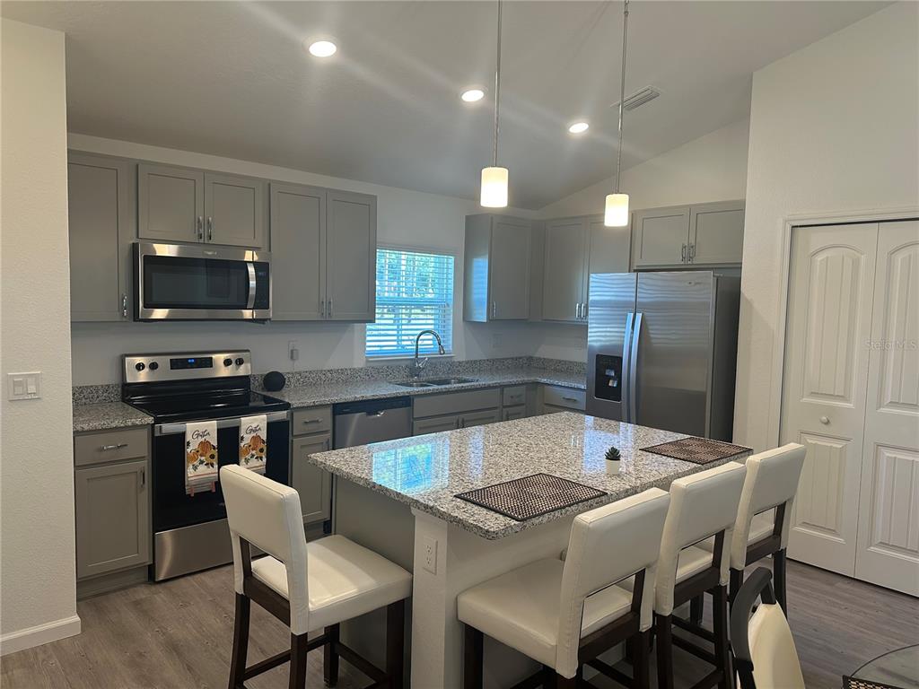 A kitchen features gray cabinets, granite countertops, a center island, and stainless steel appliances — 30 PIEDMONT DRIVE, PALM COAST, FL