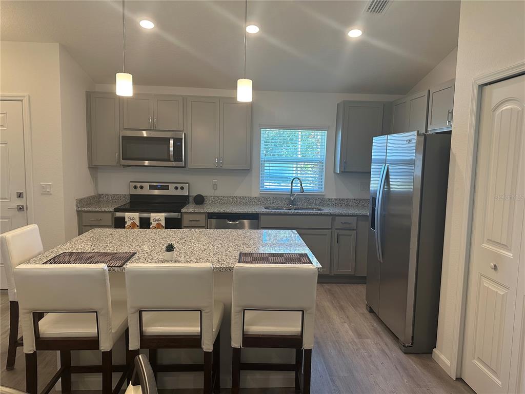 A kitchen features gray cabinets, granite countertops, stainless steel appliances, and a central island — 30 PIEDMONT DRIVE, PALM COAST, FL