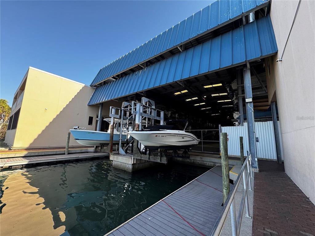 Two boats are docked on lifts inside a covered marina structure next to a building — 408 GULF OF MEXICO DRIVE UNIT 2112, LONGBOAT KEY, FL