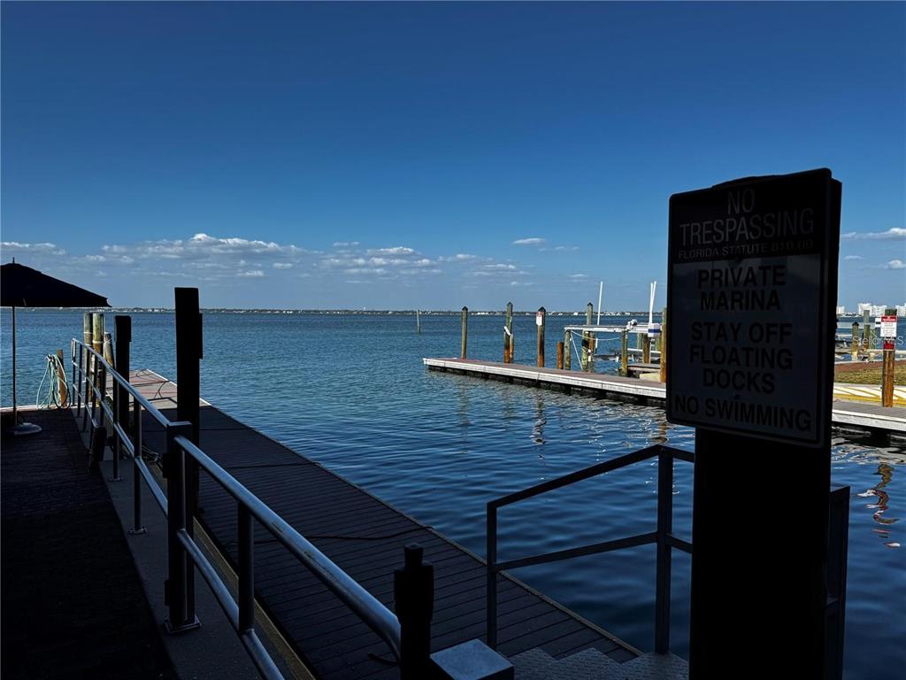 A wooden dock with metal railings extends into a calm bay under a blue sky — 408 GULF OF MEXICO DRIVE UNIT 2112, LONGBOAT KEY, FL