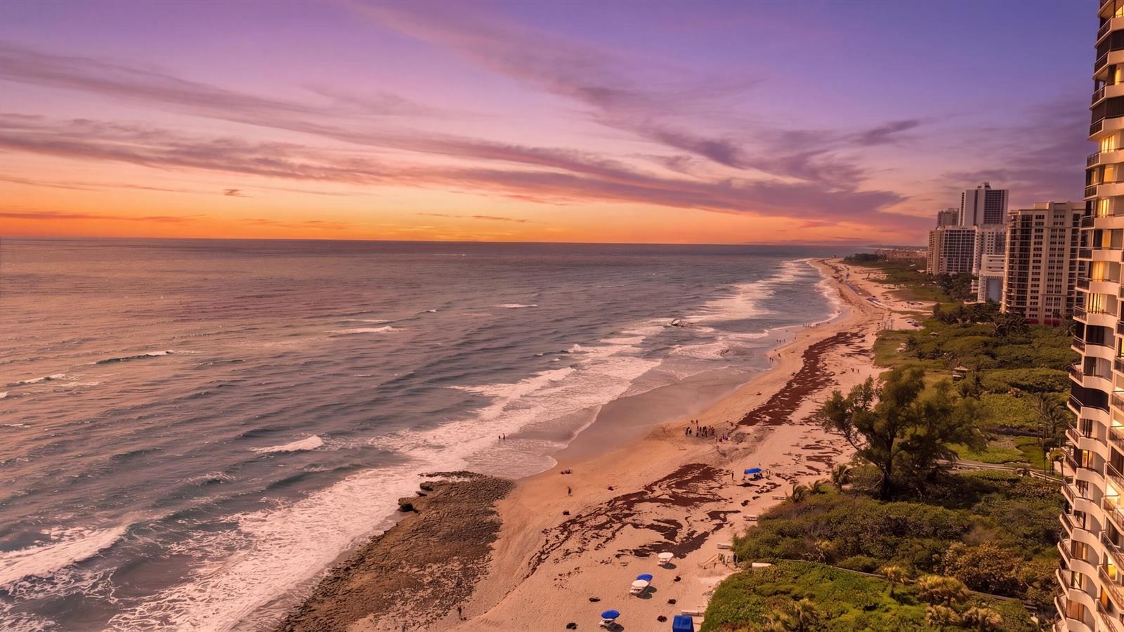 An aerial view of a sandy beach at sunset next to high-rise residential buildings — 3972 N Ocean Drive # 5, Singer Island FL 33404, SINGER ISLAND, FL