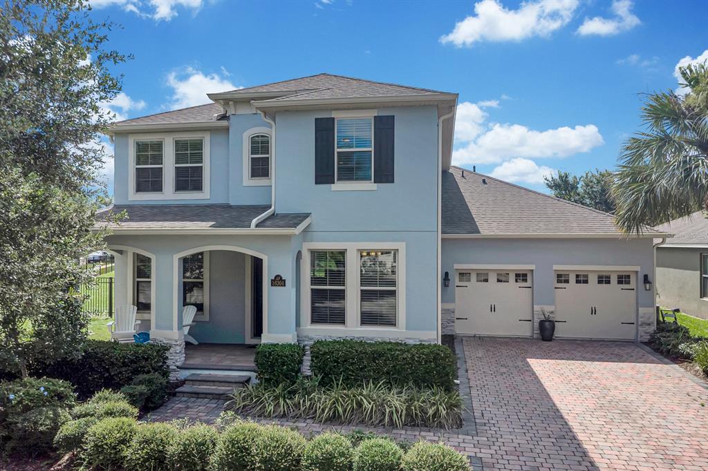 A two-story light blue house with a brick driveway, two-car garage, and covered front porch — 16304 WIND VIEW LANE, WINTER GARDEN, FL