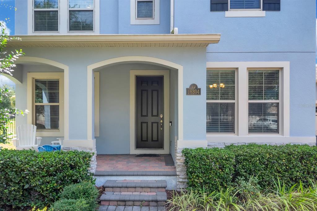 The front entrance of a two-story blue house features a dark door and stone steps — 16304 WIND VIEW LANE, WINTER GARDEN, FL