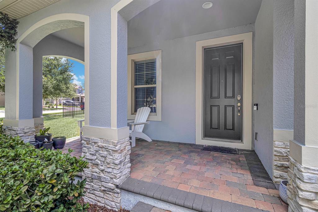 A covered front porch features stone-based columns, a brick paver floor, and a dark front door — 16304 WIND VIEW LANE, WINTER GARDEN, FL