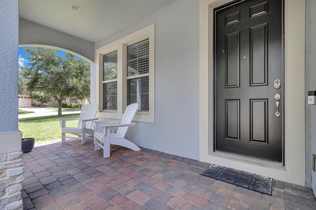 A covered front porch features brick pavers, two white Adirondack chairs, and a black front door — 16304 WIND VIEW LANE, WINTER GARDEN, FL