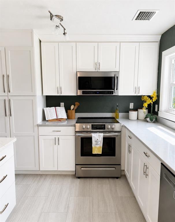 A kitchen features white cabinets, stainless steel appliances, a dark backsplash, and light-colored flooring — 926 29TH STREET N, ST PETERSBURG, FL