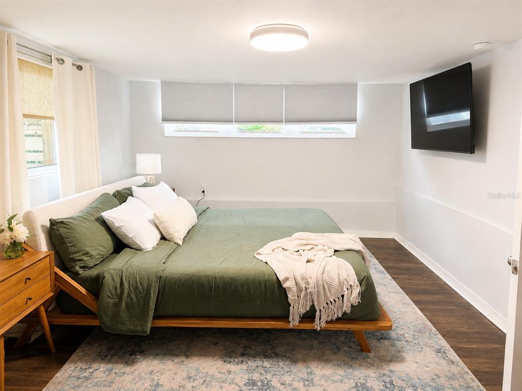 A bedroom features a platform bed with green bedding, a wall-mounted television, and wood flooring — 926 29TH STREET N, ST PETERSBURG, FL
