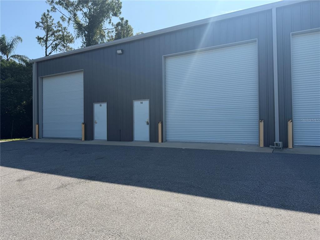 The exterior of a gray metal warehouse building features two roll-up doors and two entry doors — 5475 DOVE DRIVE UNIT 15, NEW PORT RICHEY, FL
