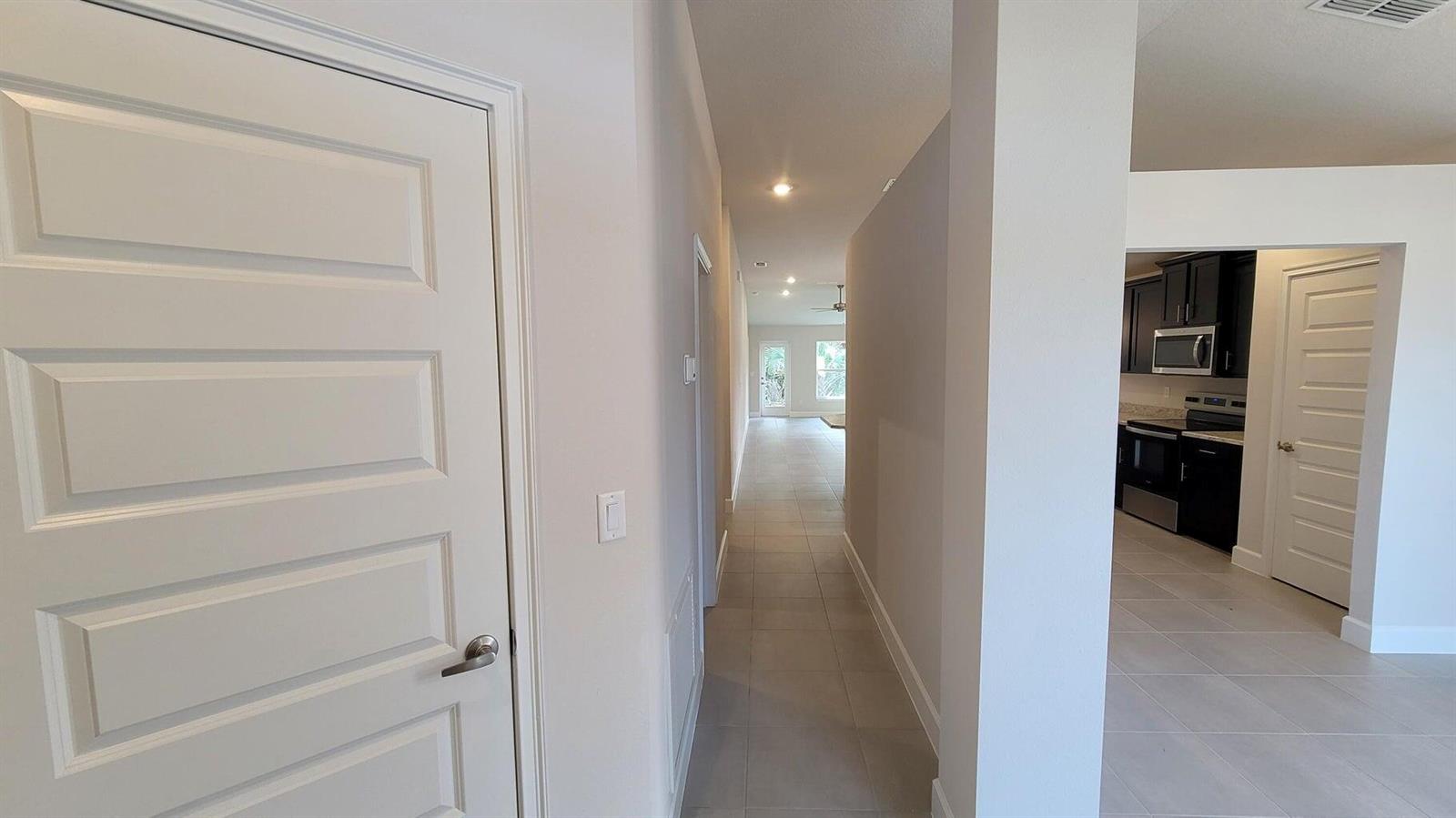 A hallway with tile flooring leads toward a bright living area past a kitchen entrance — 8802 Waterstone Boulevard, Fort Pierce FL 34951, FORT PIERCE, FL