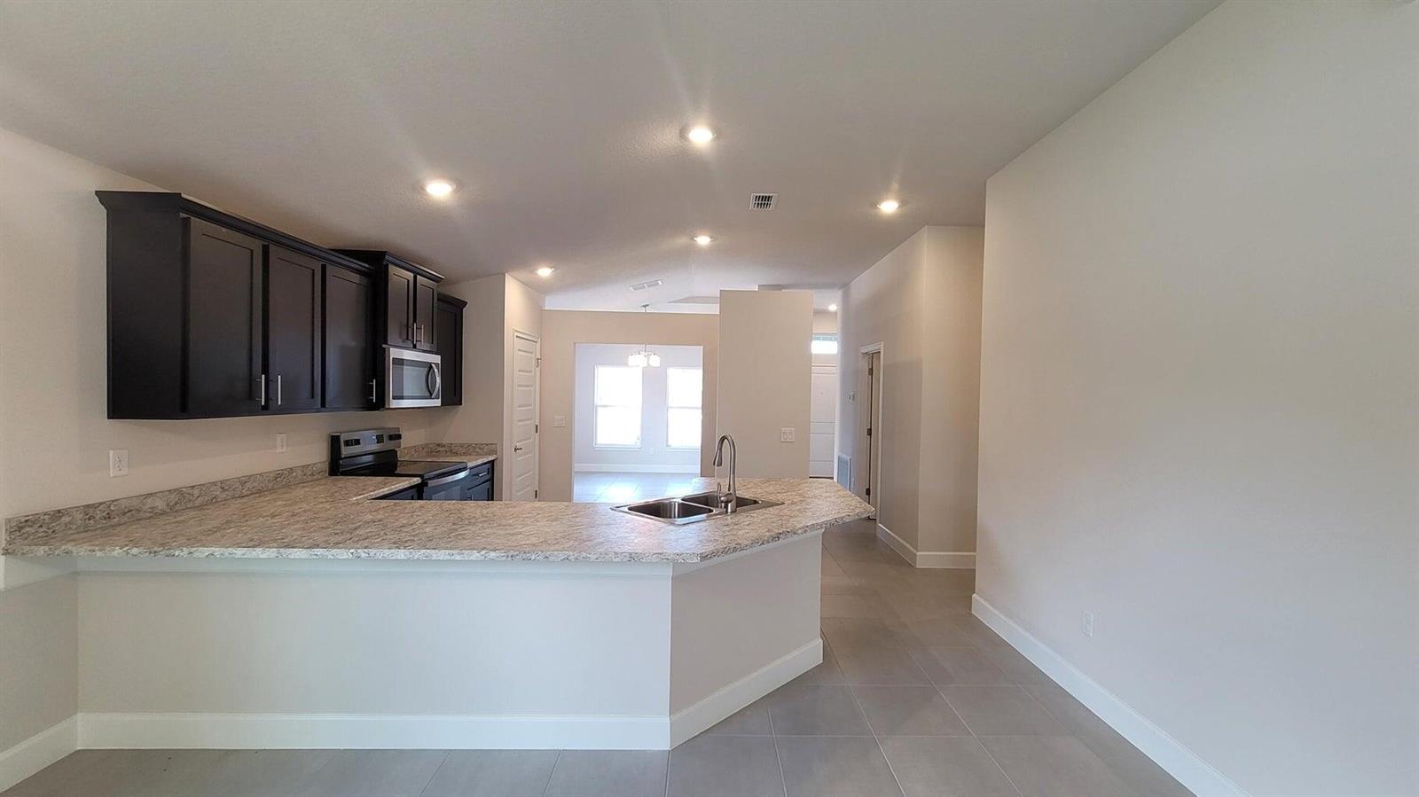 A kitchen with dark cabinets, granite countertops, and a peninsula island overlooks a living area — 8802 Waterstone Boulevard, Fort Pierce FL 34951, FORT PIERCE, FL