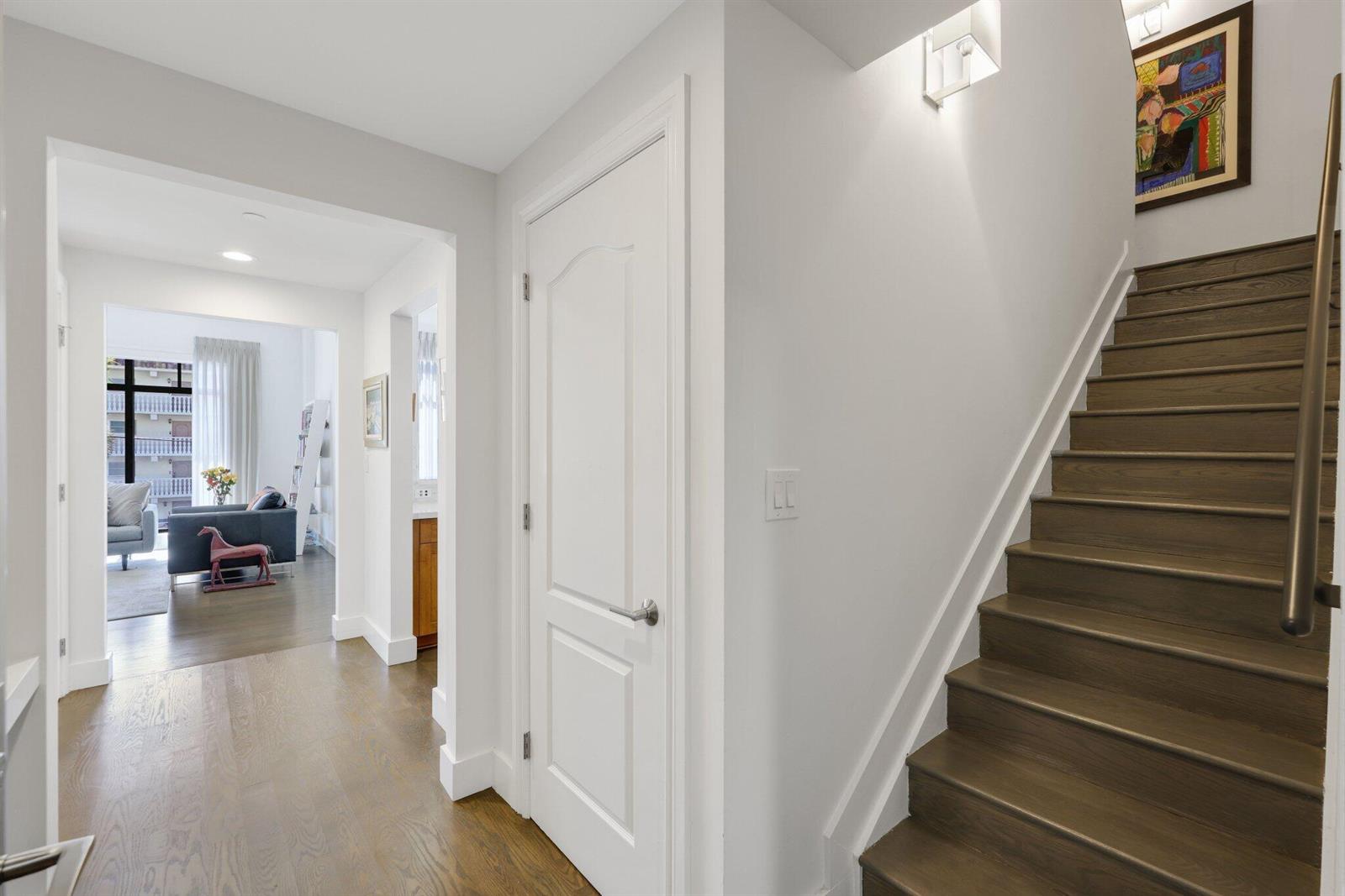A hallway with hardwood floors leads to a living area past a white door and staircase — 200 E Palmetto Park Road # 7, Boca Raton FL 33432, BOCA RATON, FL