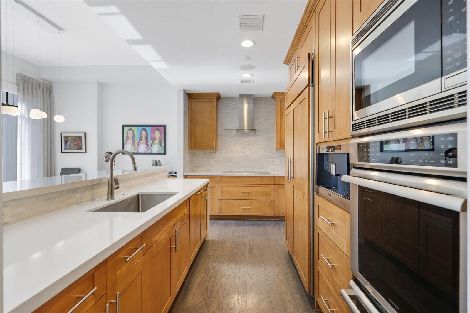 A modern kitchen features light wood cabinetry, white countertops, stainless steel appliances, and hardwood floors — 200 E Palmetto Park Road # 7, Boca Raton FL 33432, BOCA RATON, FL