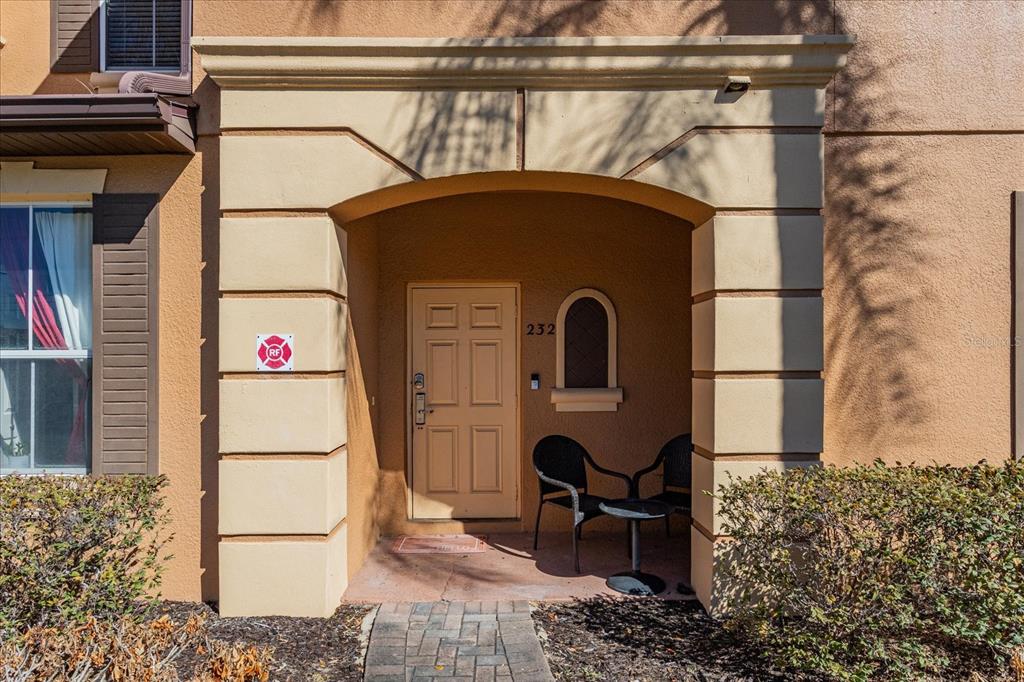 The exterior entrance of a home features a tan door, arched niche, and two chairs — 232 LA MIRAGE STREET, DAVENPORT, FL