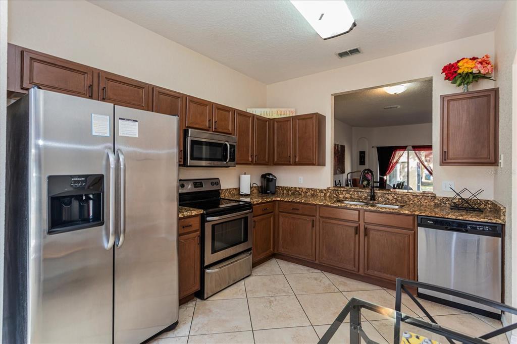 A kitchen features stainless steel appliances, wood cabinets, and granite countertops with tile flooring — 232 LA MIRAGE STREET, DAVENPORT, FL