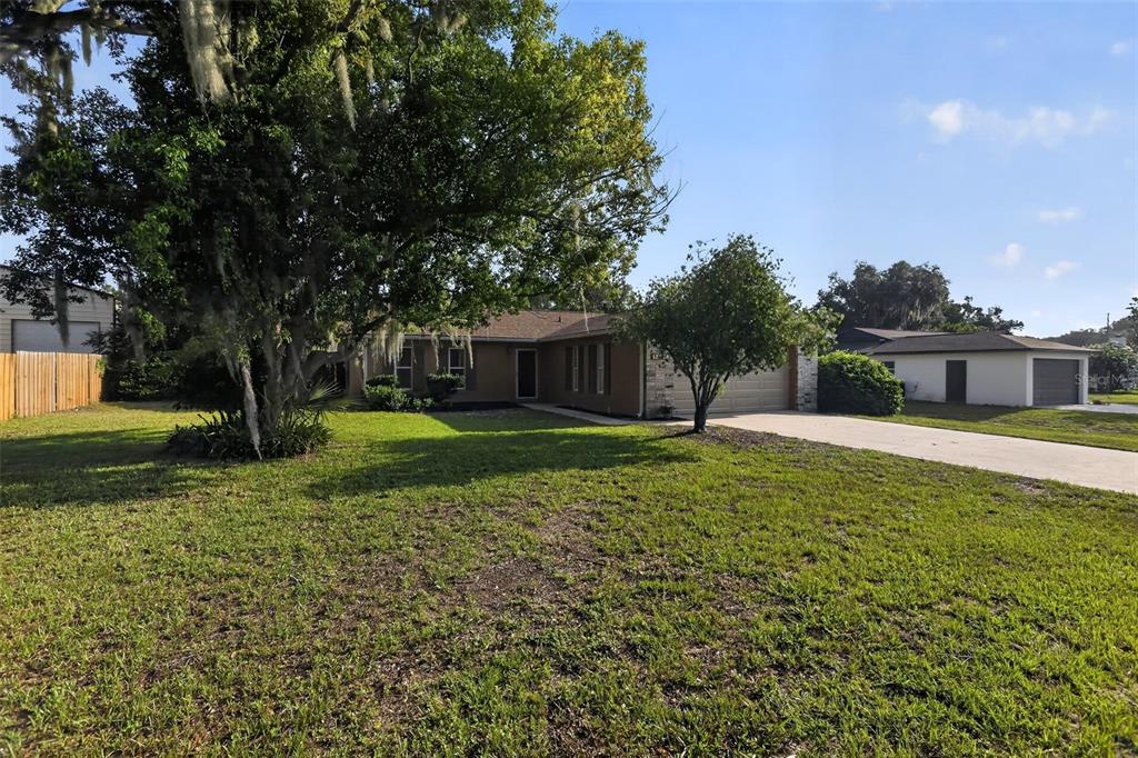 A single-story house with a tan exterior, a concrete driveway, and large trees in the yard — 13635 BERKSHIRE COURT, GRAND ISLAND, FL