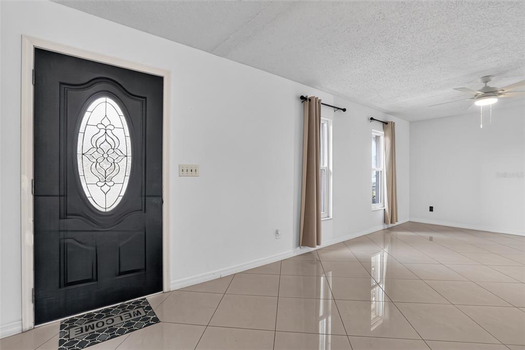 An entryway with a black front door, light tile flooring, and two windows with curtains — 13635 BERKSHIRE COURT, GRAND ISLAND, FL