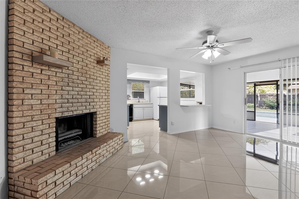 A living room with a brick fireplace, tile flooring, and an opening to the kitchen — 13635 BERKSHIRE COURT, GRAND ISLAND, FL
