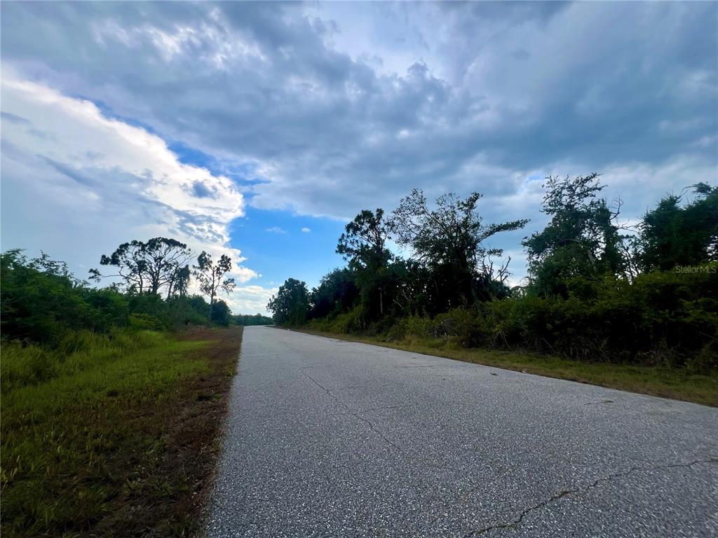 A paved road stretches through a rural area with trees and a cloudy sky — 7370 SIOUX STREET, PORT CHARLOTTE, FL