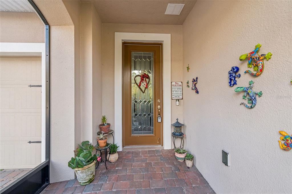 A brown front door with a glass insert sits on a brick porch with potted plants — 795 AVIARA LANE, KISSIMMEE, FL