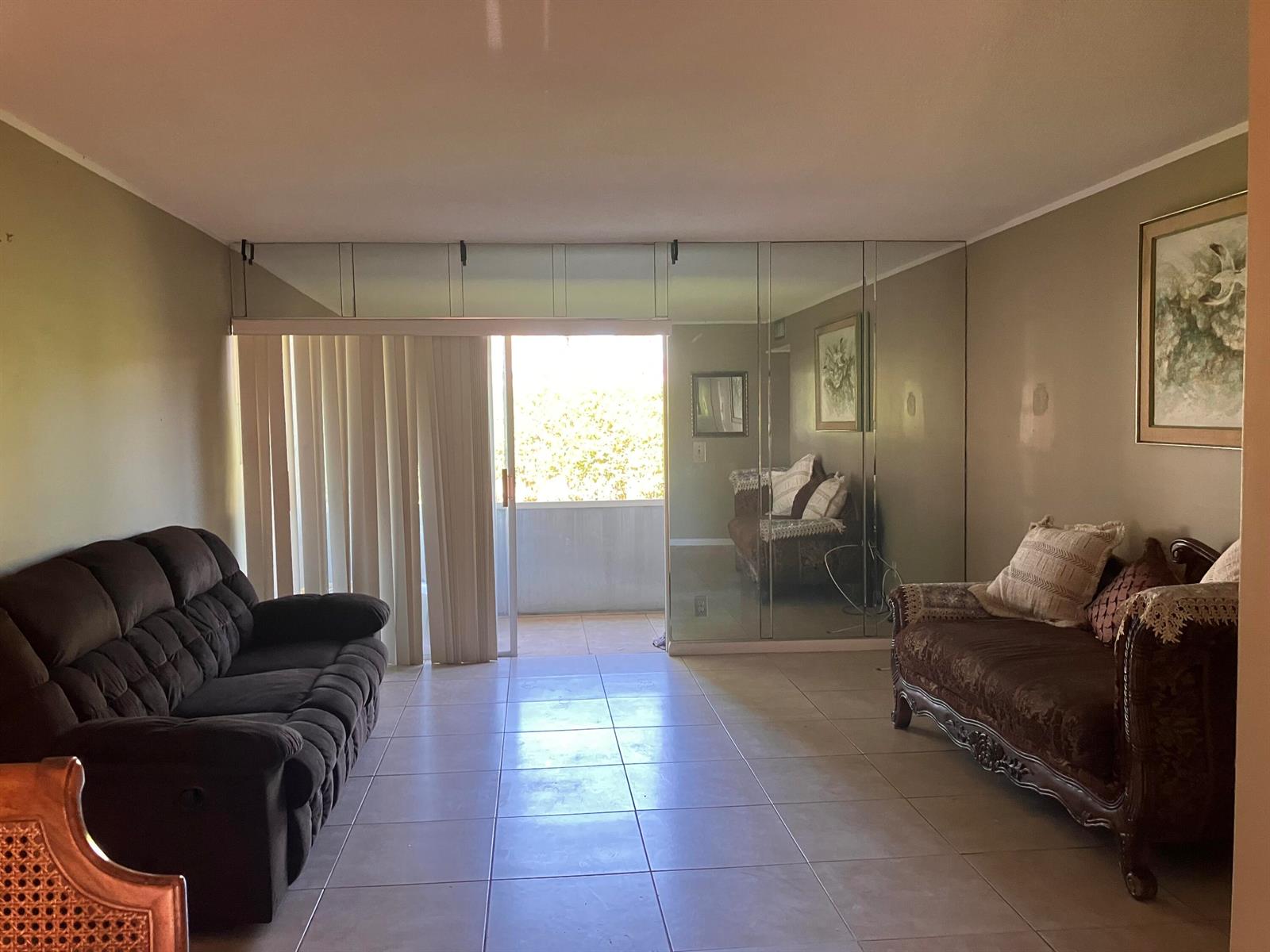 A living room features tiled floors, a mirrored wall, and a sliding glass door to a balcony — 17 Golfs Edge # D, West Palm Beach FL 33417, WEST PALM BEACH, FL