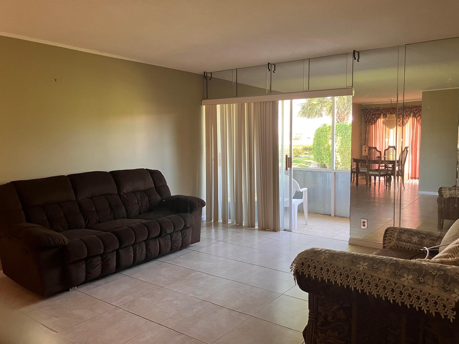 A living room features a brown sofa, tiled floors, mirrored walls, and a sliding glass door — 17 Golfs Edge # D, West Palm Beach FL 33417, WEST PALM BEACH, FL