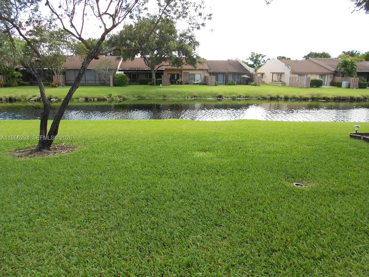A grassy lawn overlooks a narrow canal with residential townhomes in the background — 7924 NW 10th St, Plantation FL 33322, PLANTATION, FL