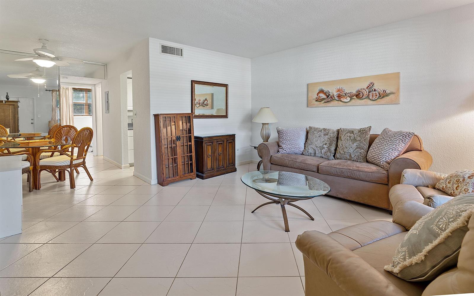 A living room with tile floors, a brown sofa, a glass coffee table, and dining area — 2565 S Ocean Boulevard # 208, Palm Beach FL 33480, PALM BEACH, FL