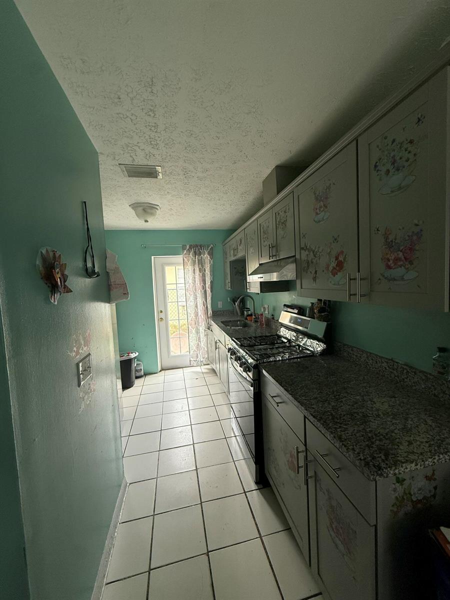 A galley kitchen features gray cabinets, granite countertops, white tile flooring, and teal walls — 14765 SW 172nd Avenue, FL 34956, FL