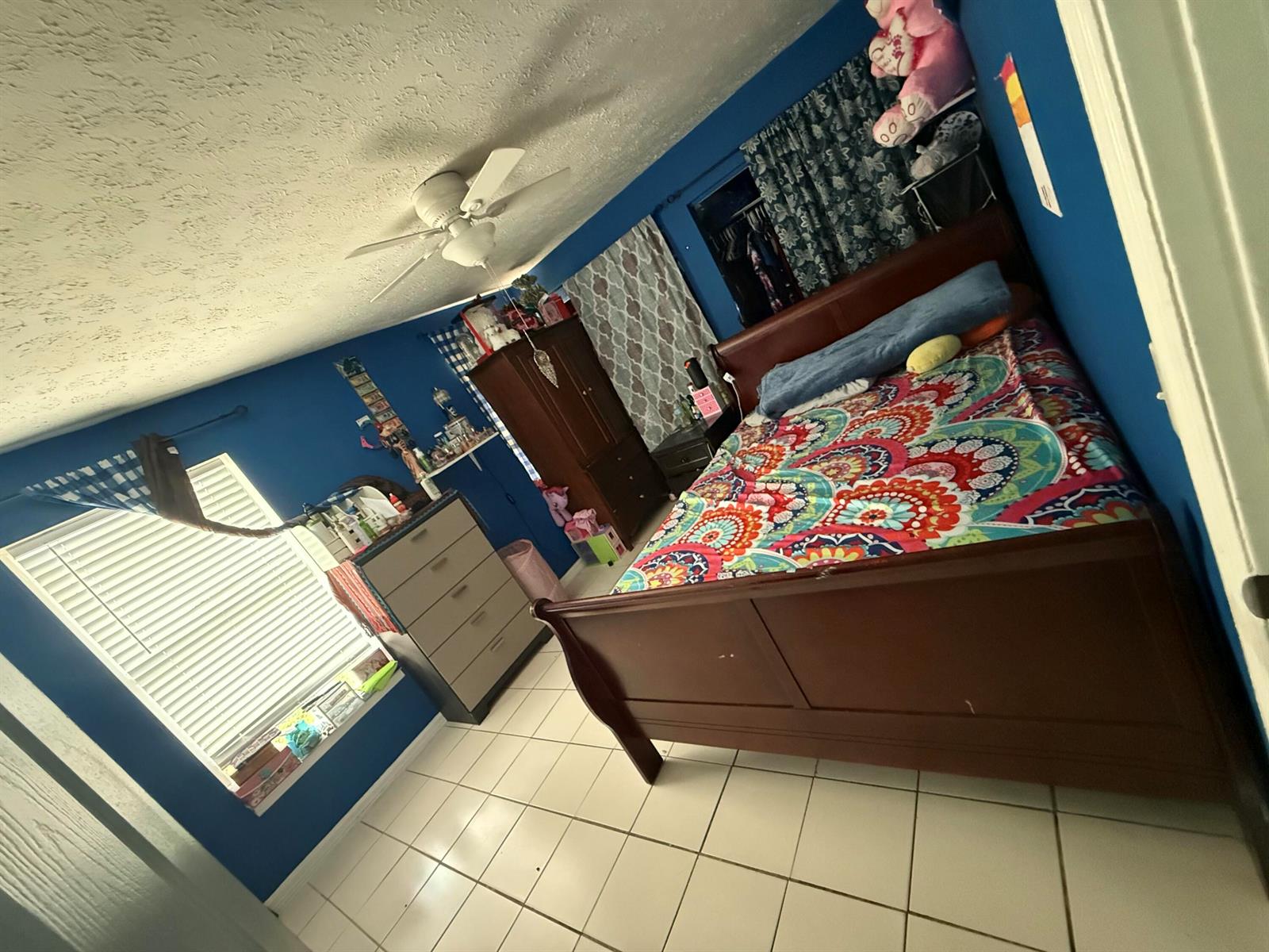 A bedroom with blue walls, a dark wood bed frame, and white tile flooring — 14765 SW 172nd Avenue, FL 34956, FL