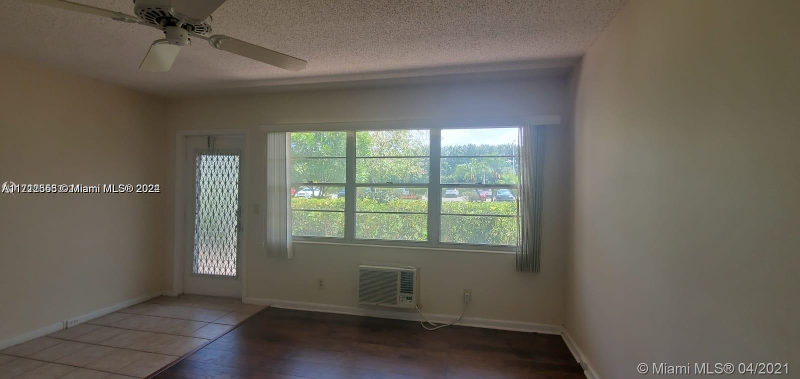 A living room features wood-look flooring, a ceiling fan, a window air conditioner, and large windows — 385 Fanshaw # J, Boca Raton FL 33434, BOCA RATON, FL