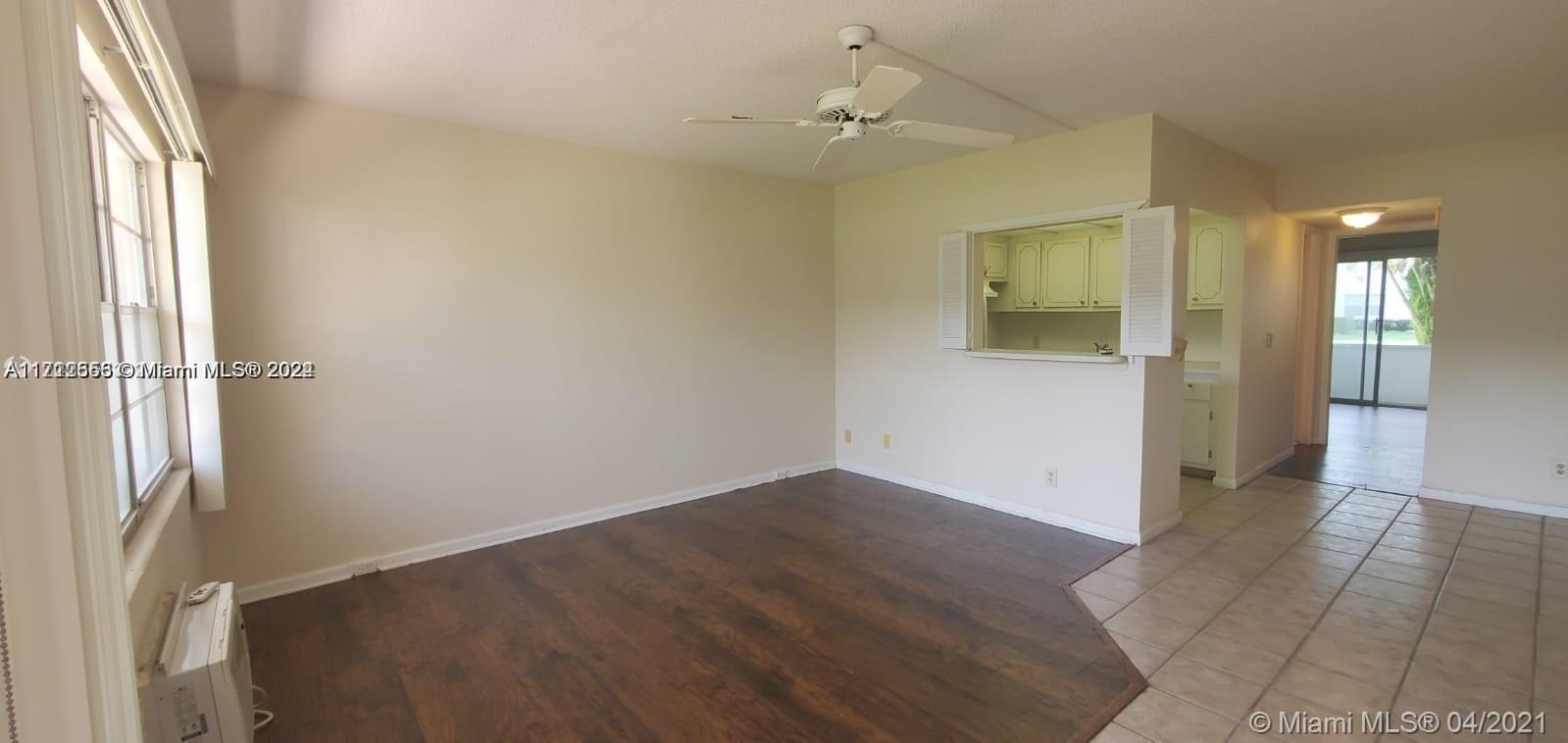 An empty living room features dark wood-look flooring, a ceiling fan, and a kitchen pass-through — 385 Fanshaw # J, Boca Raton FL 33434, BOCA RATON, FL