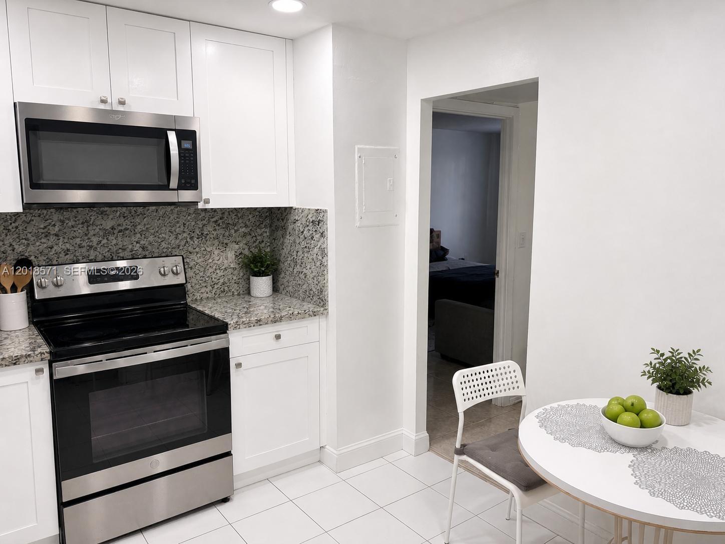 A kitchen with white cabinets, stainless steel appliances, granite countertops, and a small dining table — 1833 S Ocean Dr # 805, Hallandale Beach FL 33009, HALLANDALE BEACH, FL