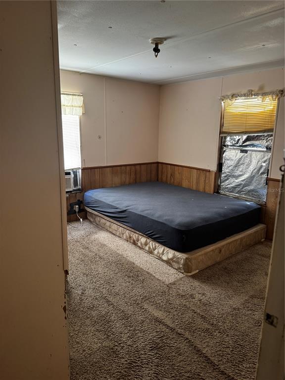 A bedroom with a mattress on the floor, wood paneling, and beige carpeting — 373 RONALD STREET, COCOA, FL