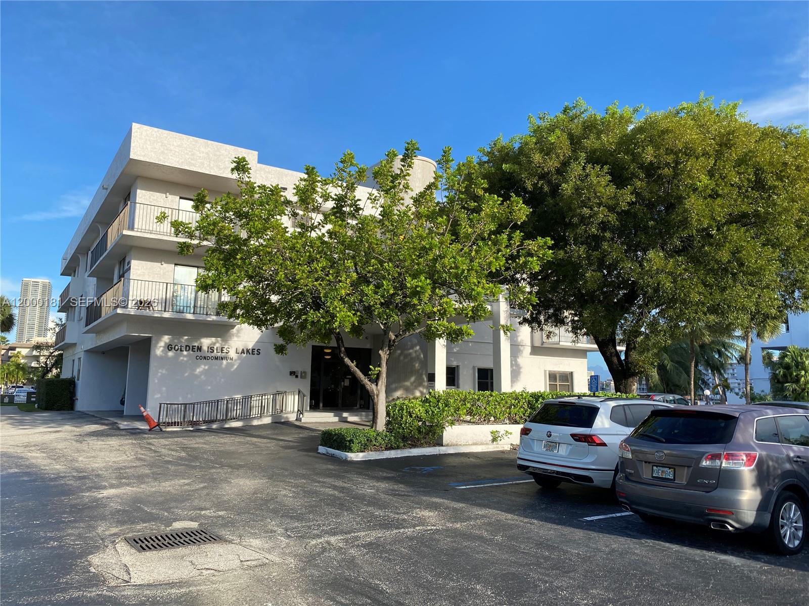 The exterior of a multi-story condominium building features a parking lot and mature trees — 1900 Diana Dr # 3D, Hallandale Beach FL 33009, HALLANDALE BEACH, FL