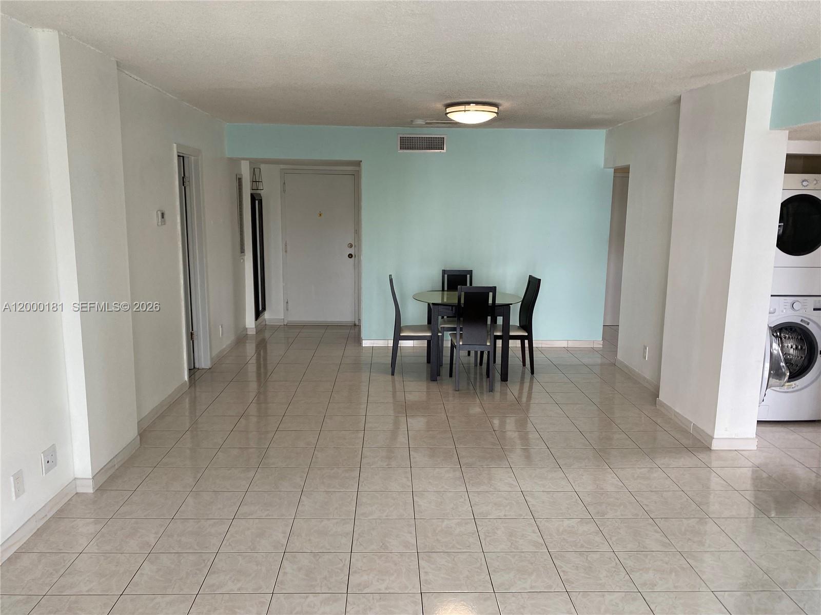 An open-concept dining area features light-colored tile flooring, a glass table, and a laundry unit — 1900 Diana Dr # 3D, Hallandale Beach FL 33009, HALLANDALE BEACH, FL