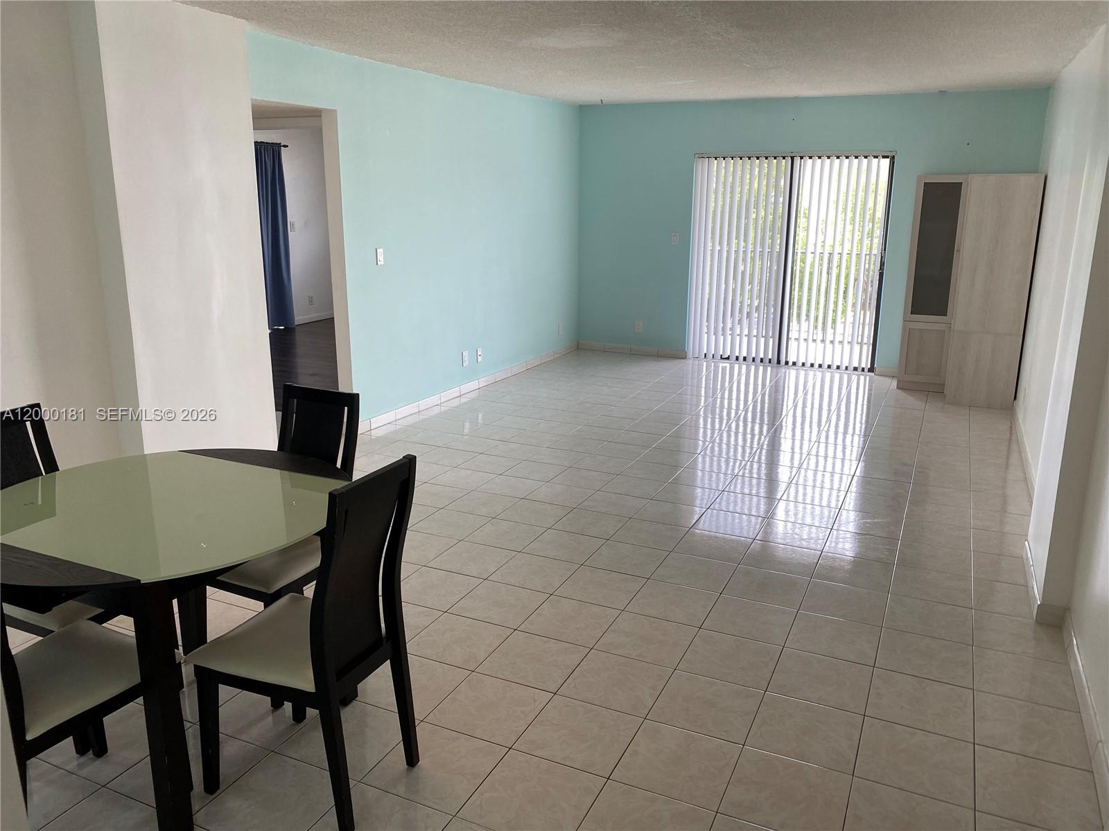 A dining area with a glass table sits beside a large, empty living room — 1900 Diana Dr # 3D, Hallandale Beach FL 33009, HALLANDALE BEACH, FL